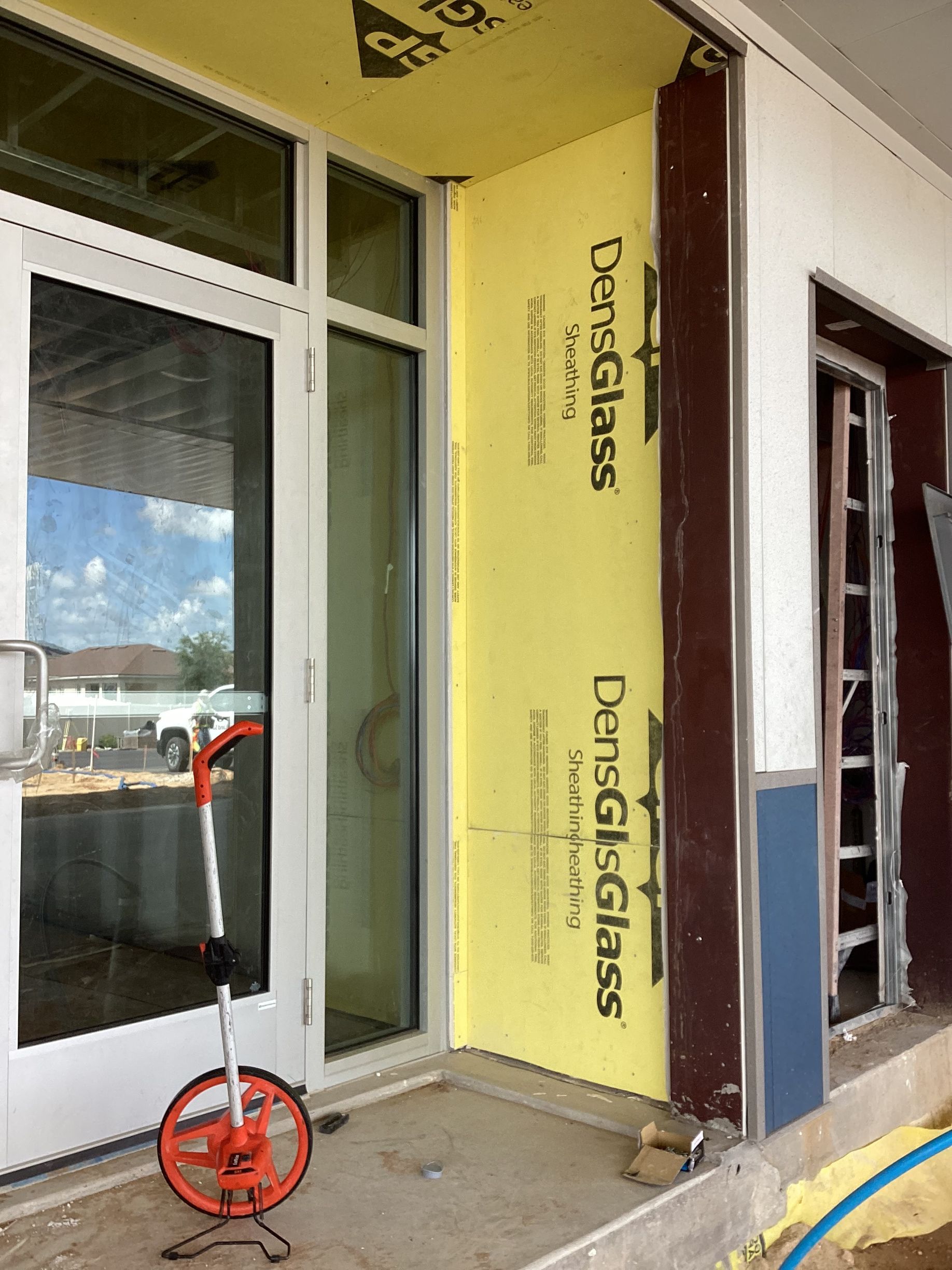 A building under construction with a yellow wall and a measuring wheel in front of it.
