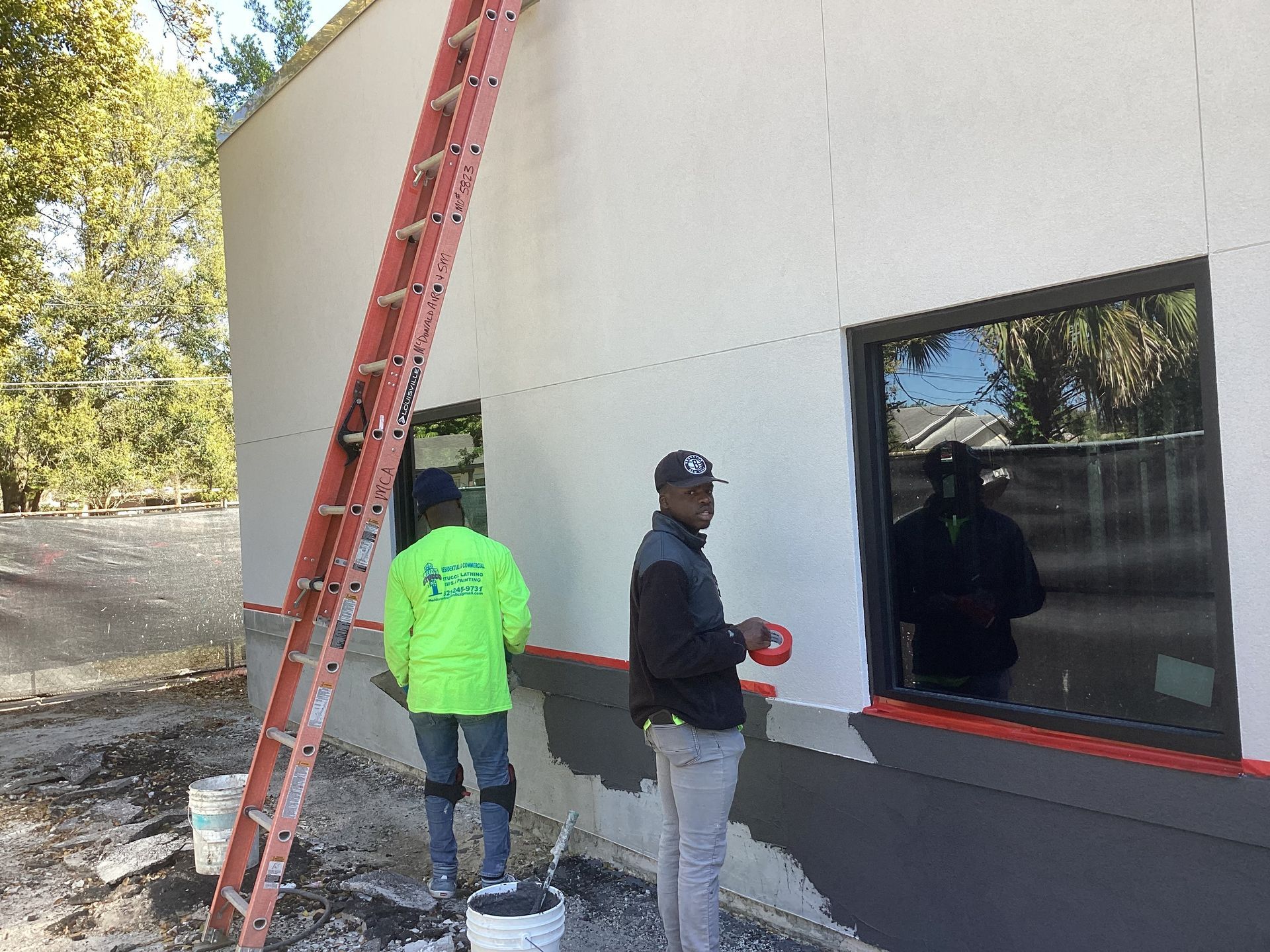 Two men are painting a building with a ladder in the background.