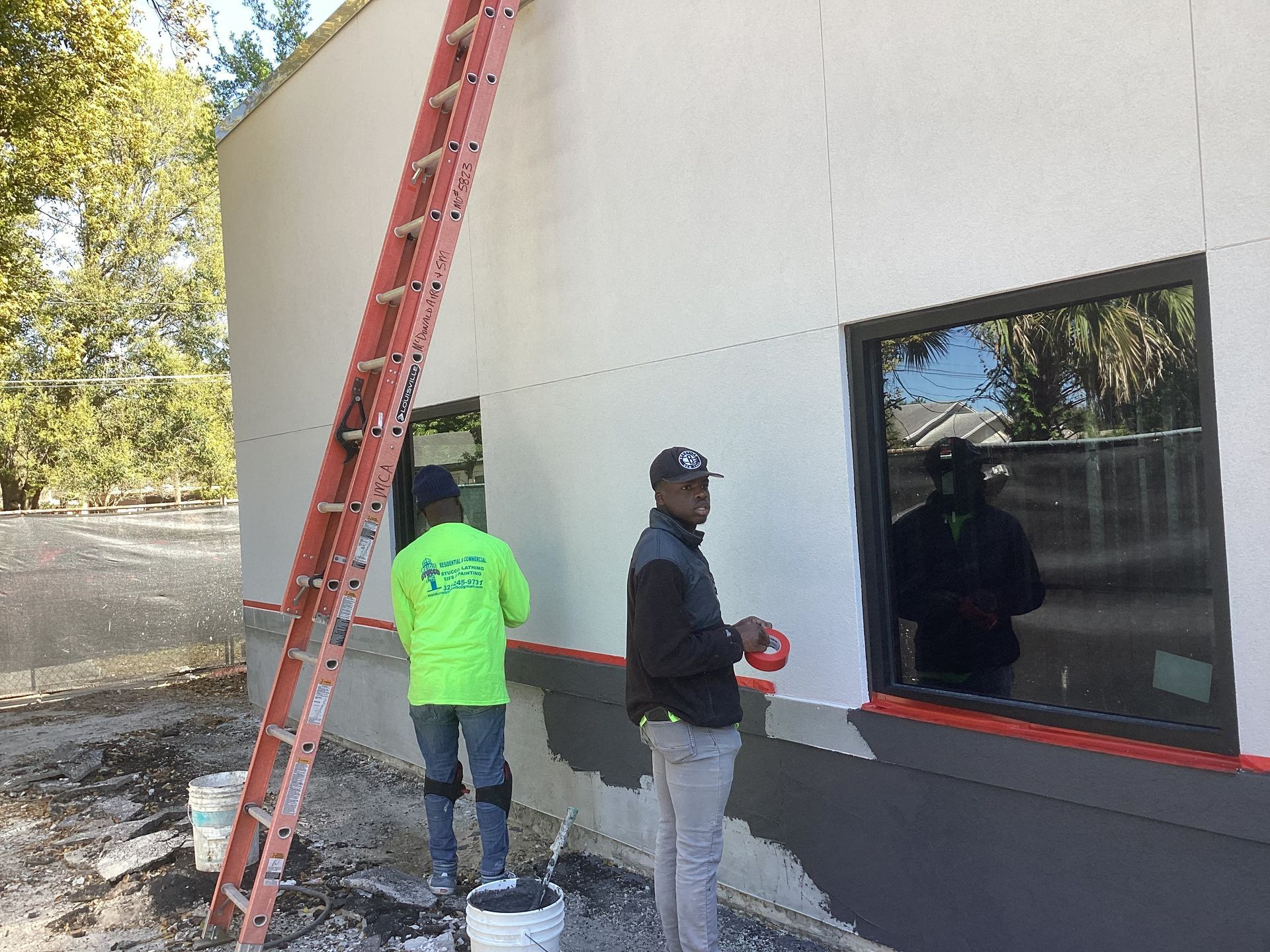 Two men are painting a building with a ladder in the background.