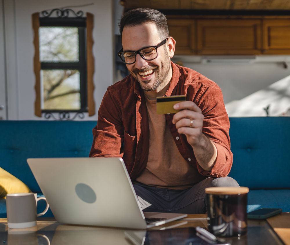 A man is sitting on a couch using a laptop and holding a credit card.