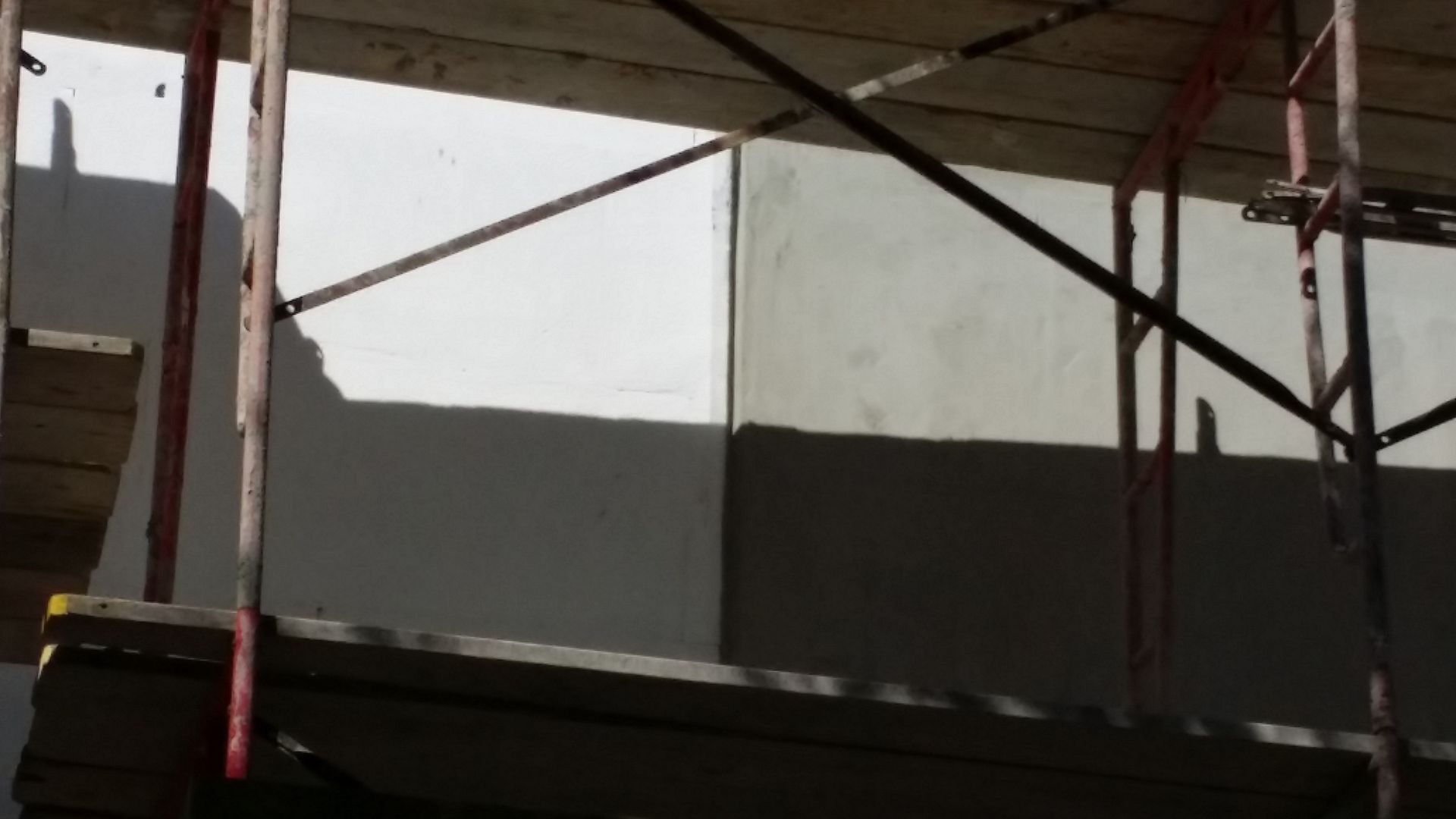 A shadow of a building is cast on a wall by a scaffolding