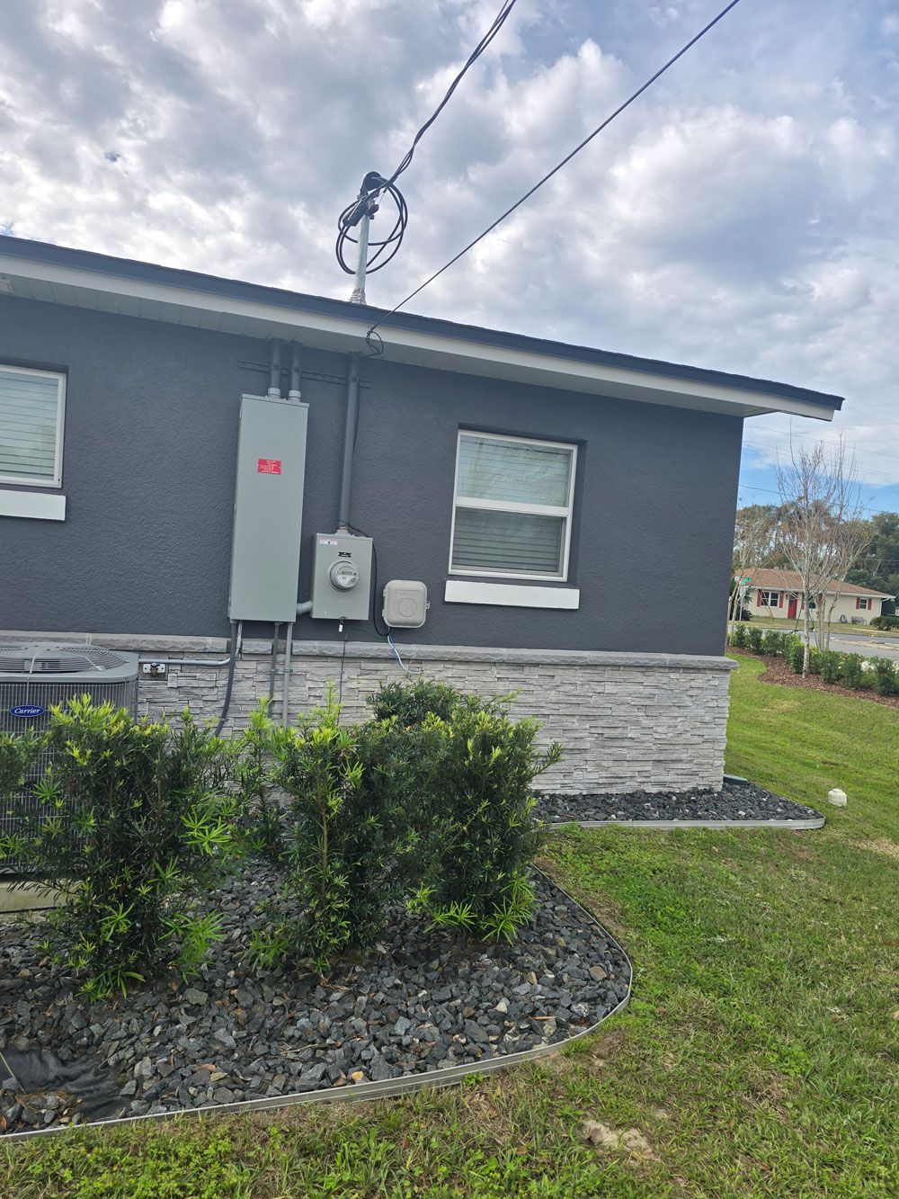 Exterior of a gray stucco building with utility boxes, a window, and a gray stone veneer base. 