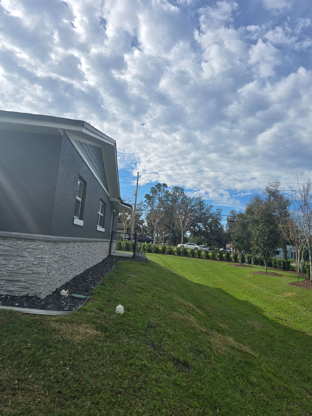 Side view of a house with dark gray siding, light brick, and a green lawn under a cloudy sky.