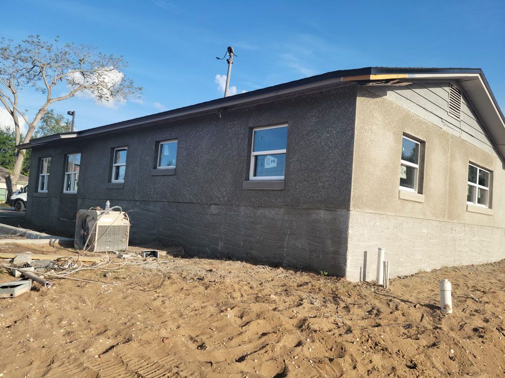 Exterior view of a stucco house under construction. Windows are installed, and the ground is dirt.