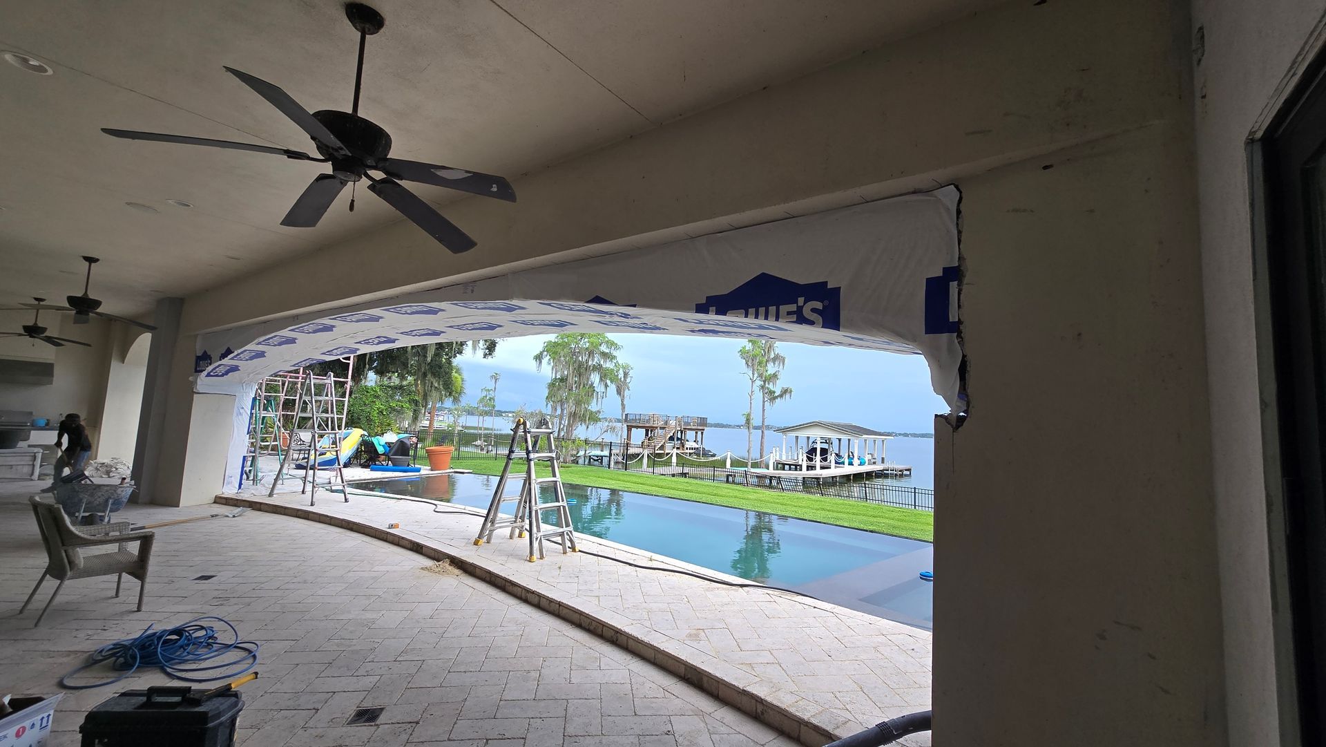 Patio with a pool, lake view, and construction in progress. An arched opening in the wall reveals the outdoor scene.