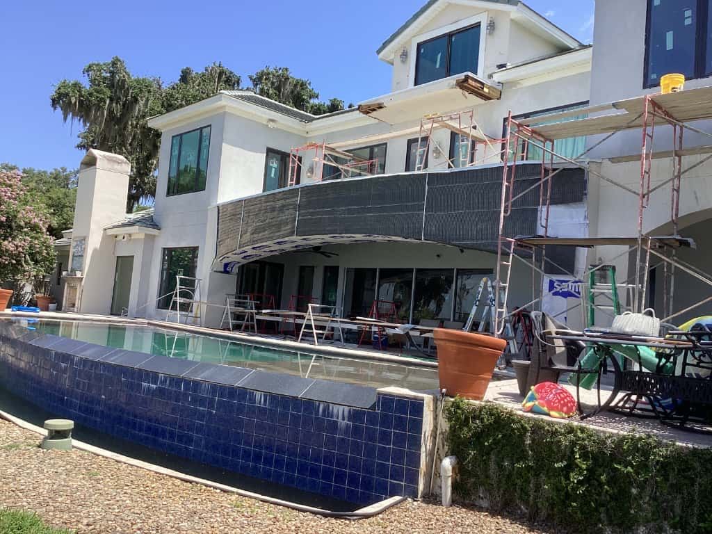 Large white house with a pool under construction, scaffolding on the balcony, and blue tiled pool.