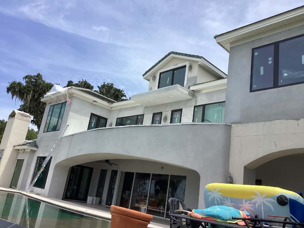 A large, light gray stucco house with a pool, arched balcony, and a blue sky.