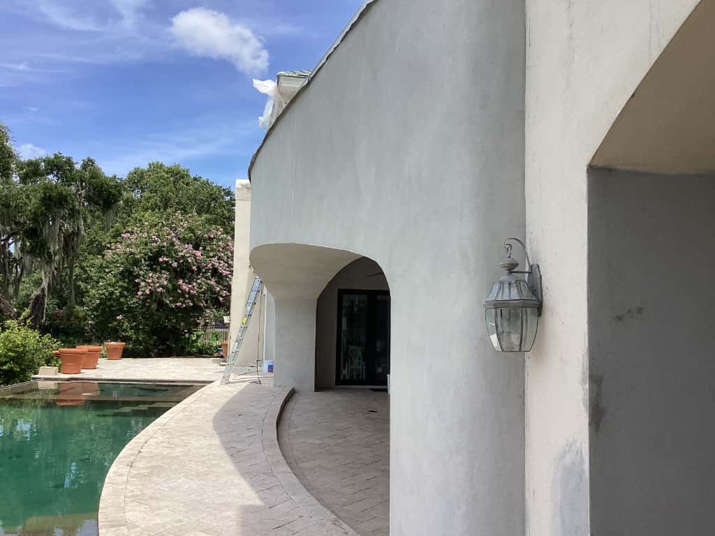 White curved building with arches overlooking a pool, surrounded by trees and a bright blue sky.