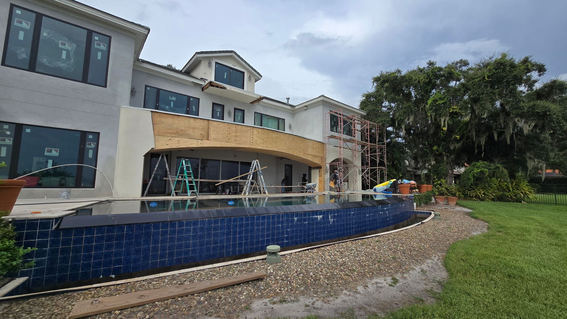 A large, multi-story house with a dark blue-tiled swimming pool in the foreground. 