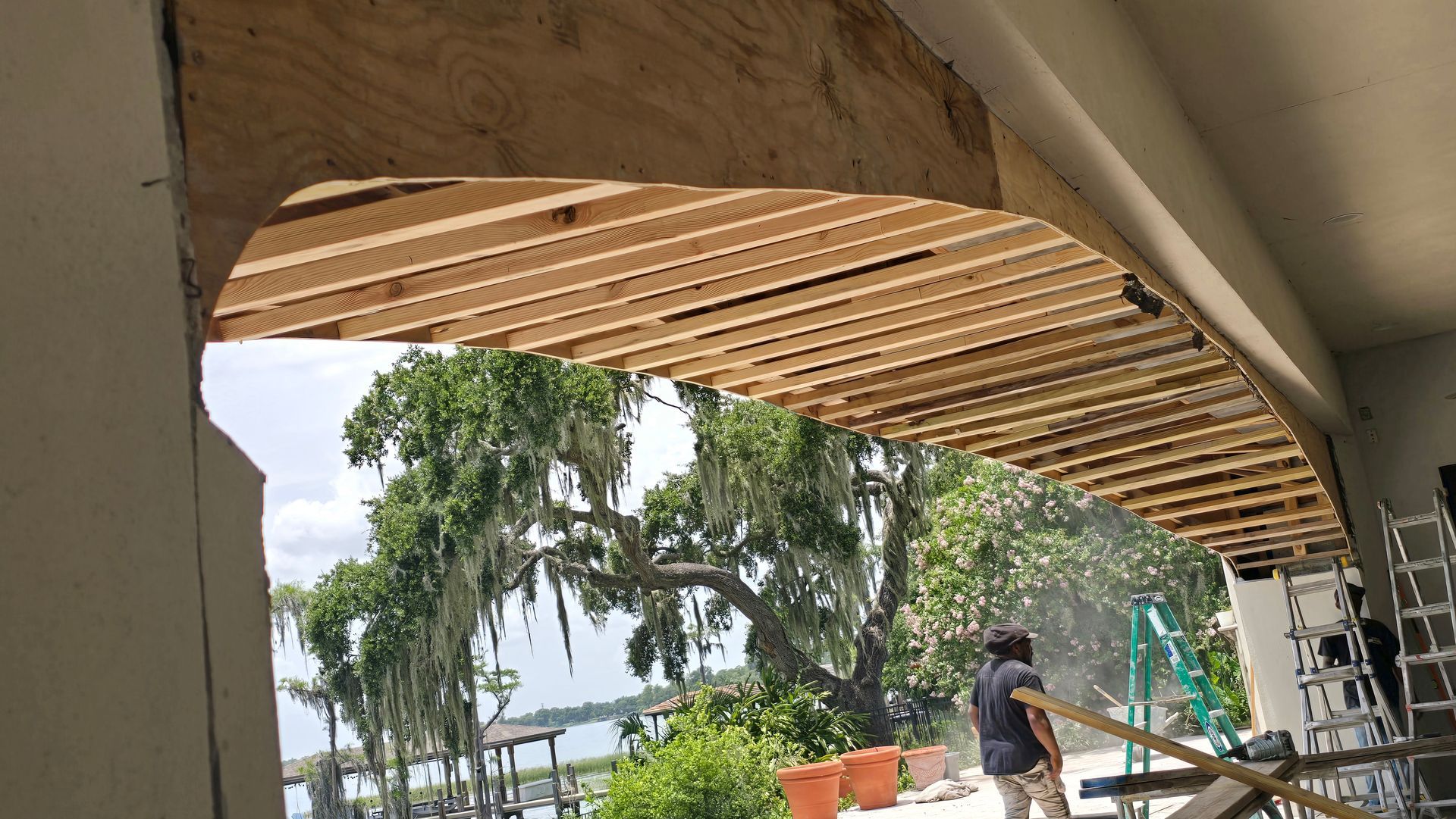 Construction of an arched entryway. Exposed wooden rafters, trees, and a man working. 