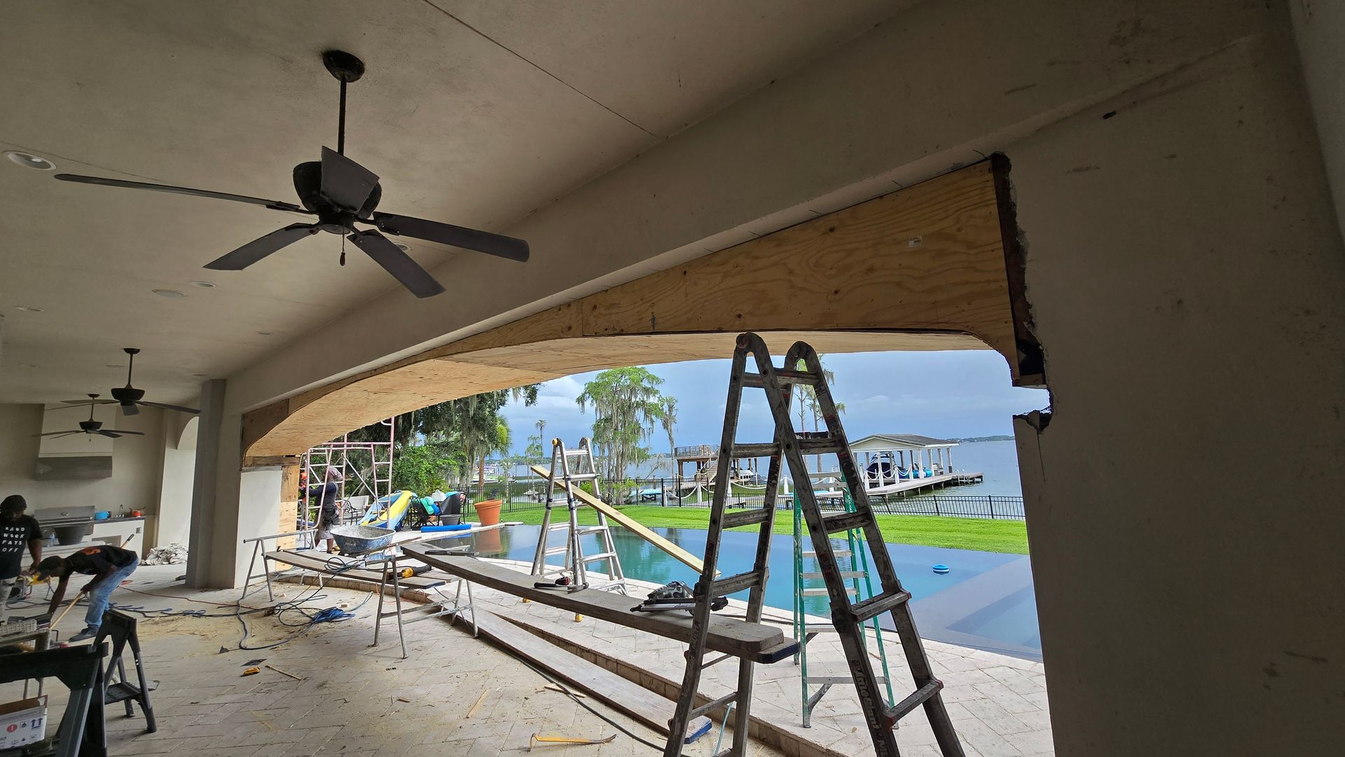 Construction site with a partially built arched doorway overlooking a pool and lake. 