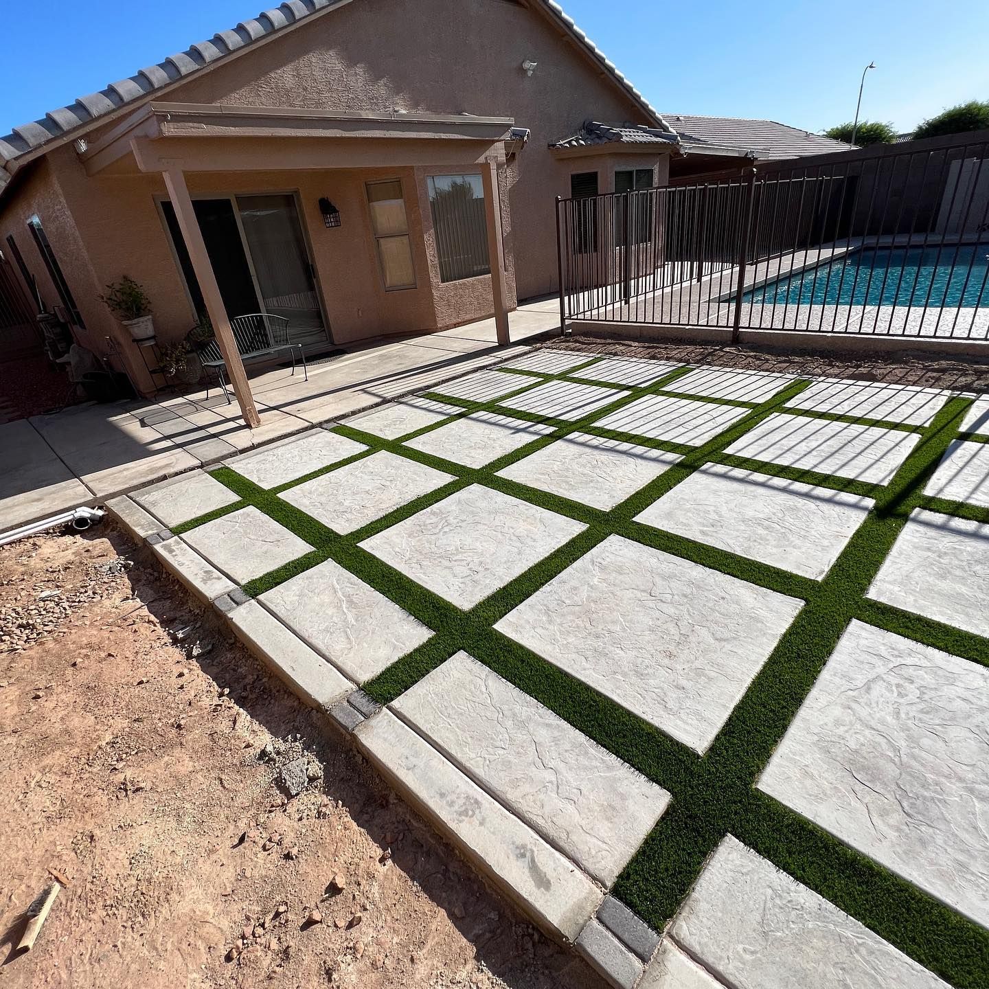 A patio with artificial grass in front of a house and a pool.