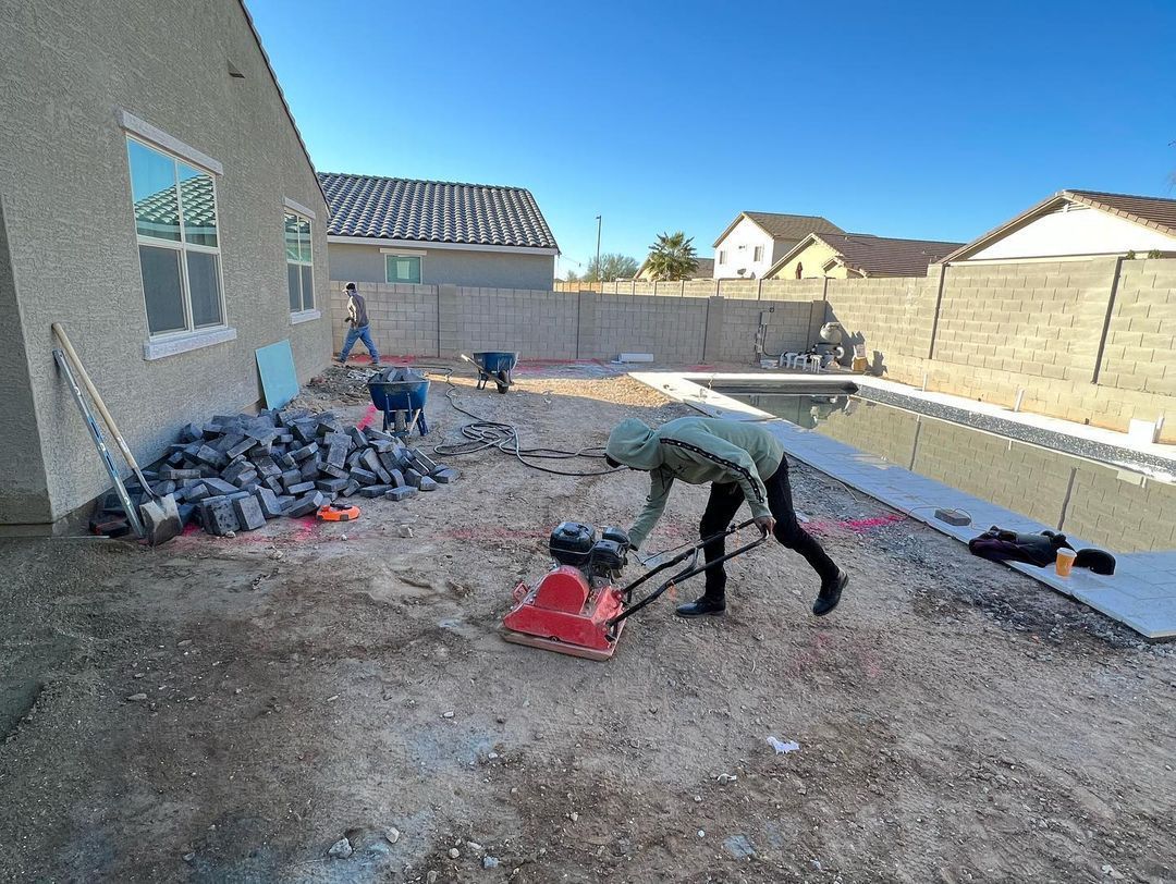 A man is standing in the dirt in front of a swimming pool.