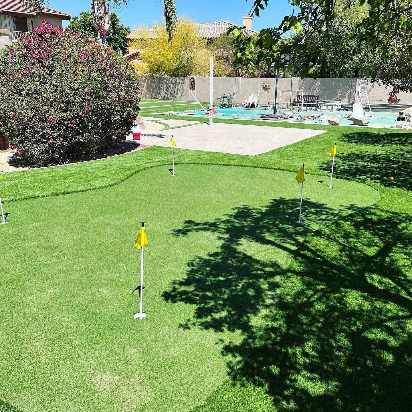 A putting green in a backyard with a pool in the background