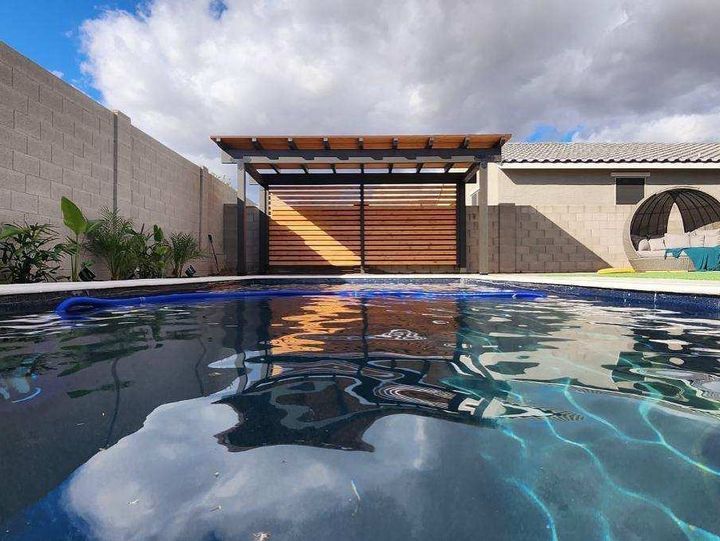 A swimming pool with a pergola and a house in the background.