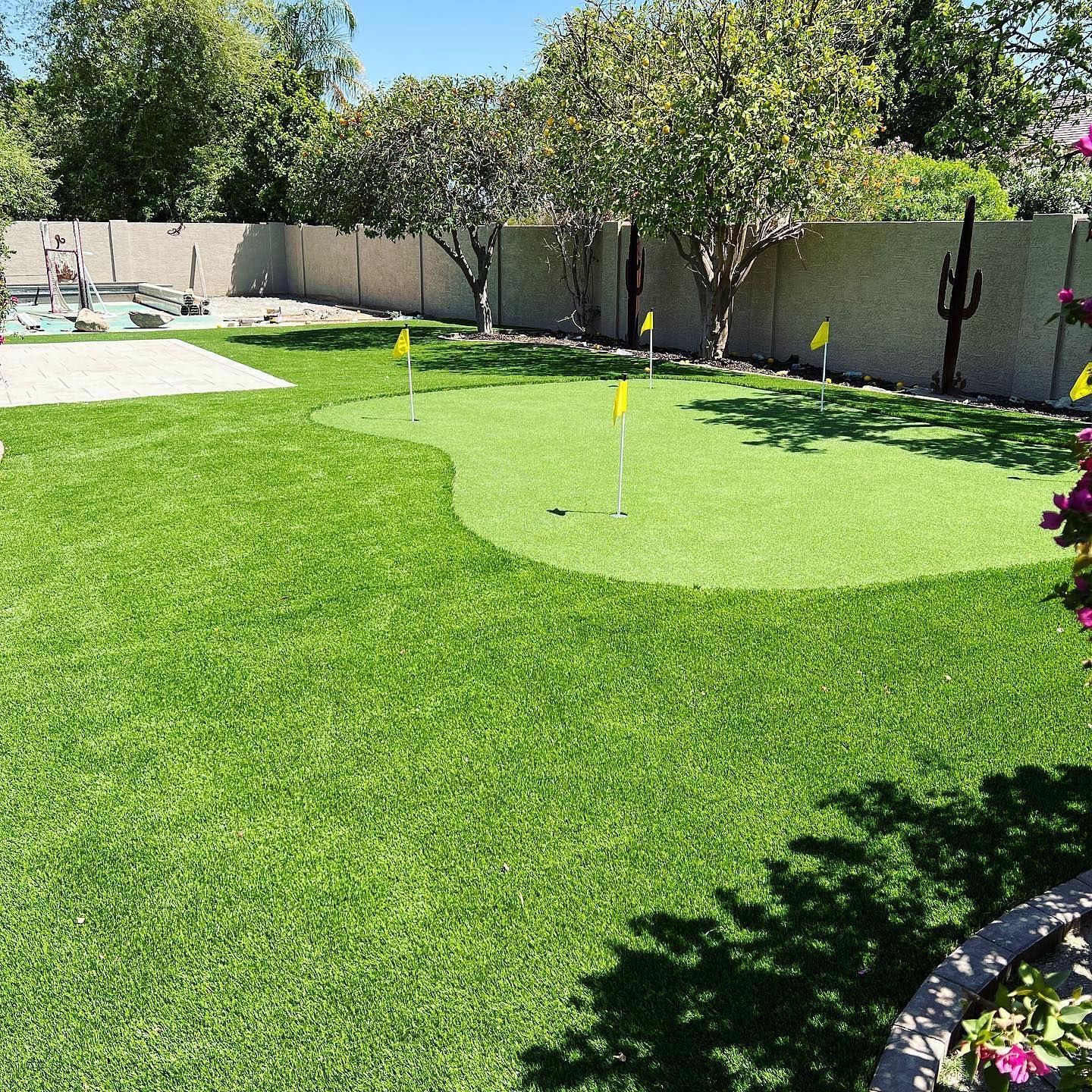 A backyard with a putting green and a pool.
