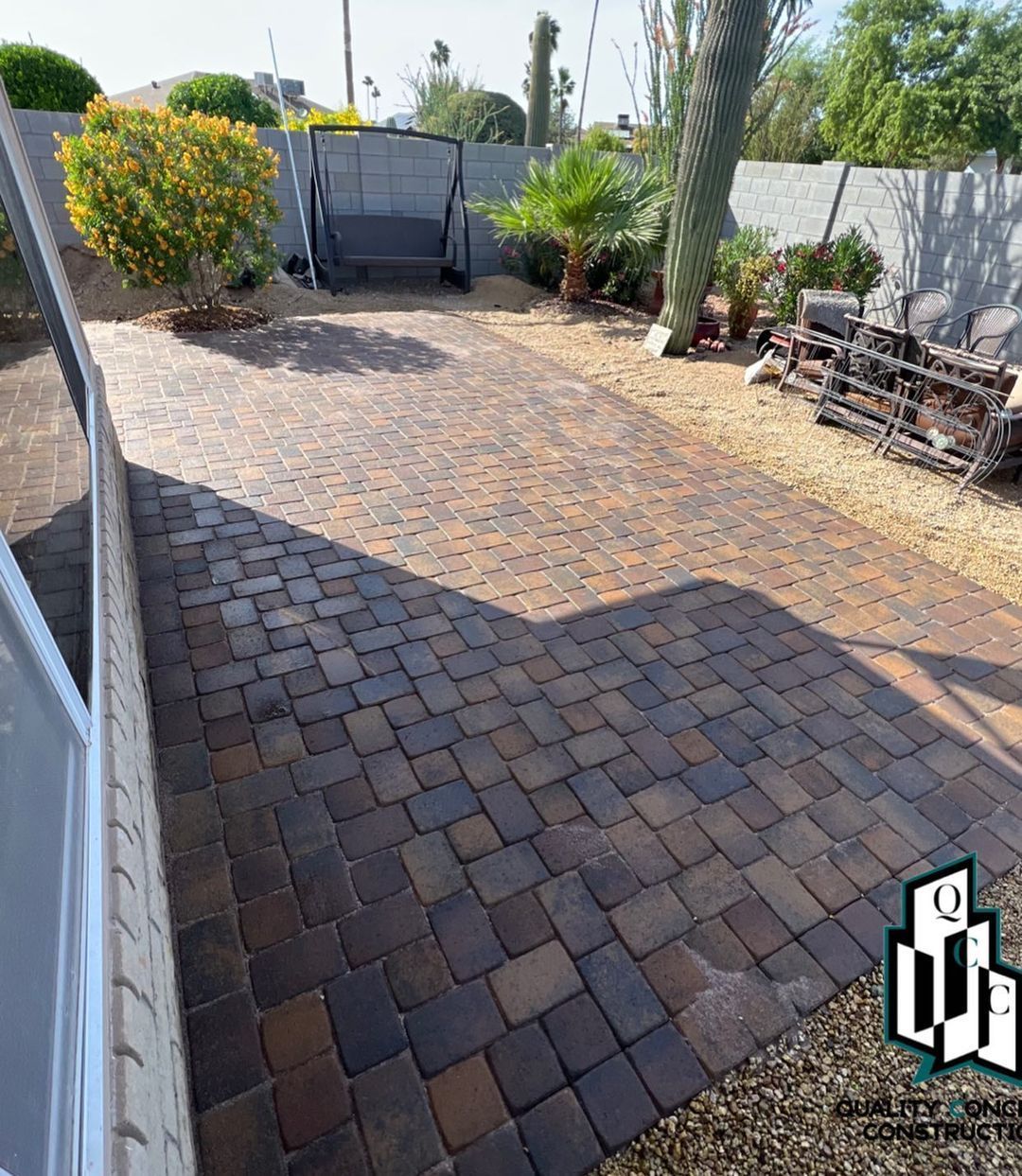 A brick driveway with a swing and a fence in the background.