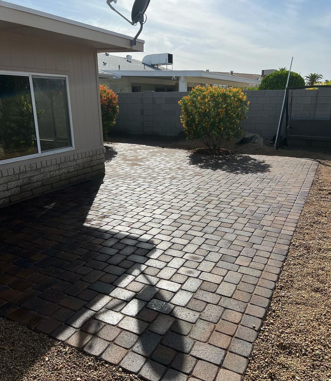 A shadow of a person is cast on a brick patio in front of a house.