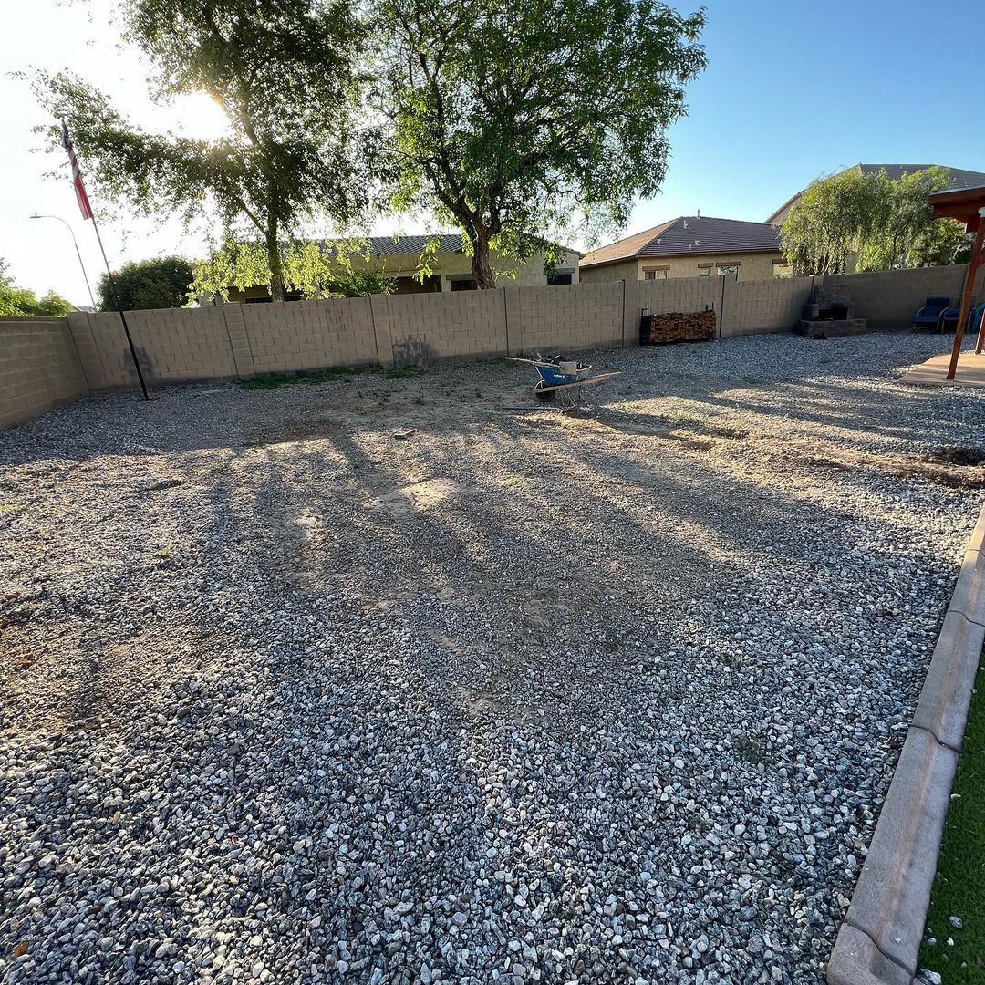 A gravel yard with a fence and trees in the background.