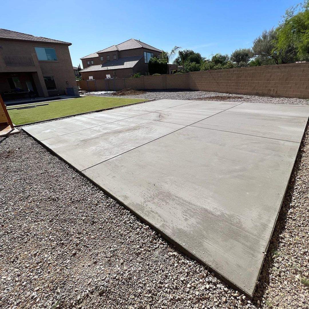 A concrete driveway in a backyard with a house in the background.