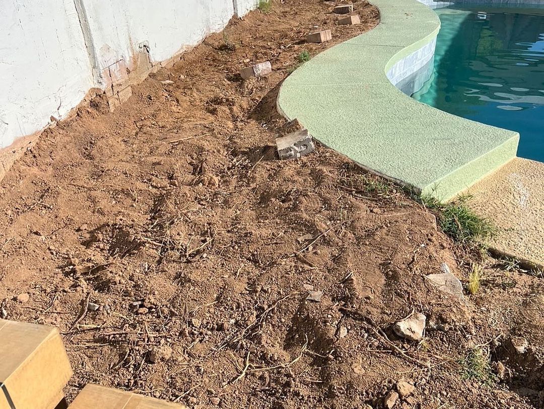 A pile of dirt is sitting next to a swimming pool.