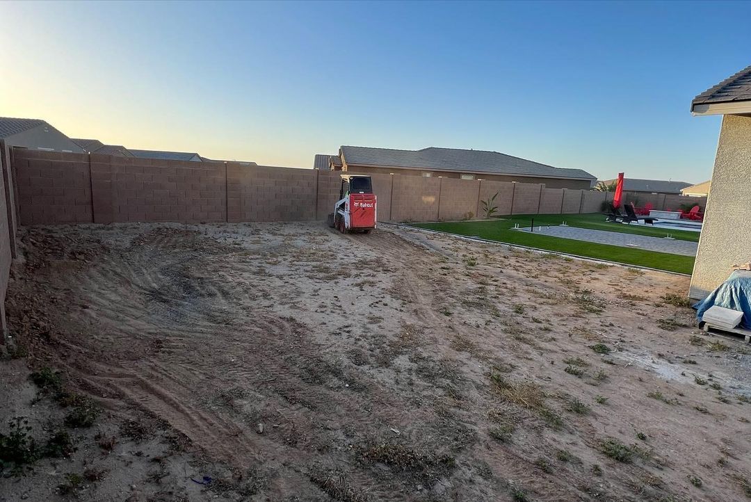 A bulldozer is driving through a dirt field in front of a house.
