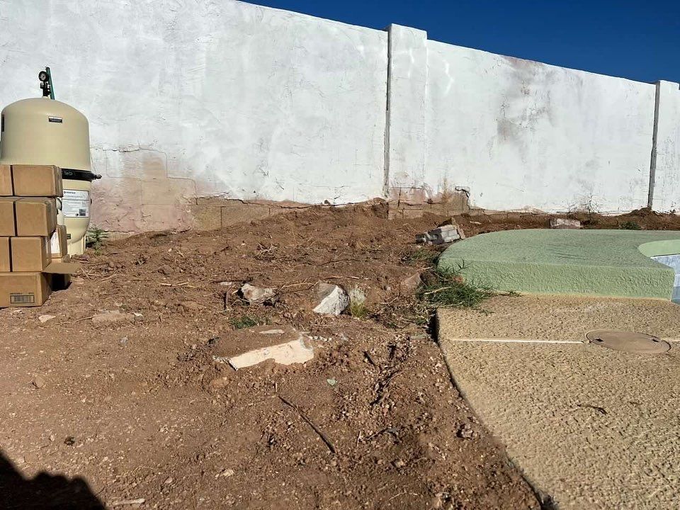 A pile of cardboard boxes sitting on top of a dirt field next to a white wall.