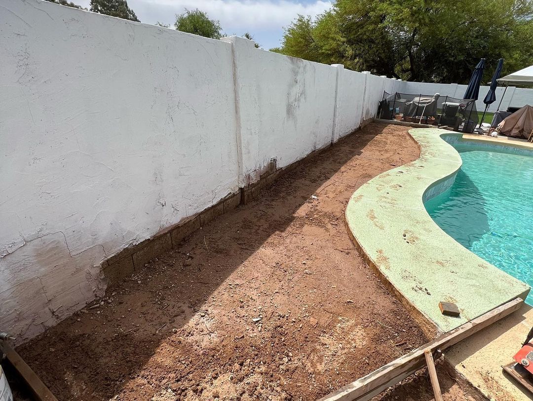 A swimming pool is being built in a backyard next to a white fence.