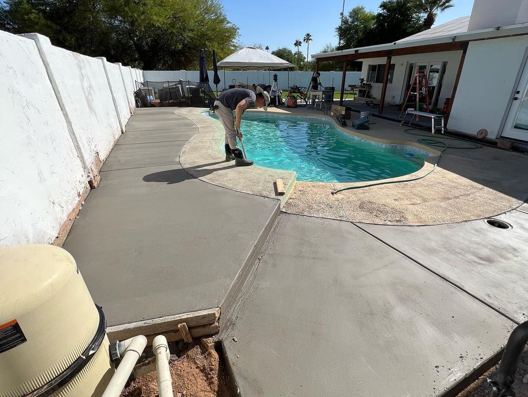A man is working on a concrete walkway around a swimming pool.
