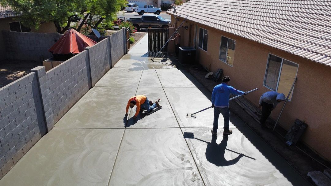 Two men are working on a concrete driveway in front of a house.