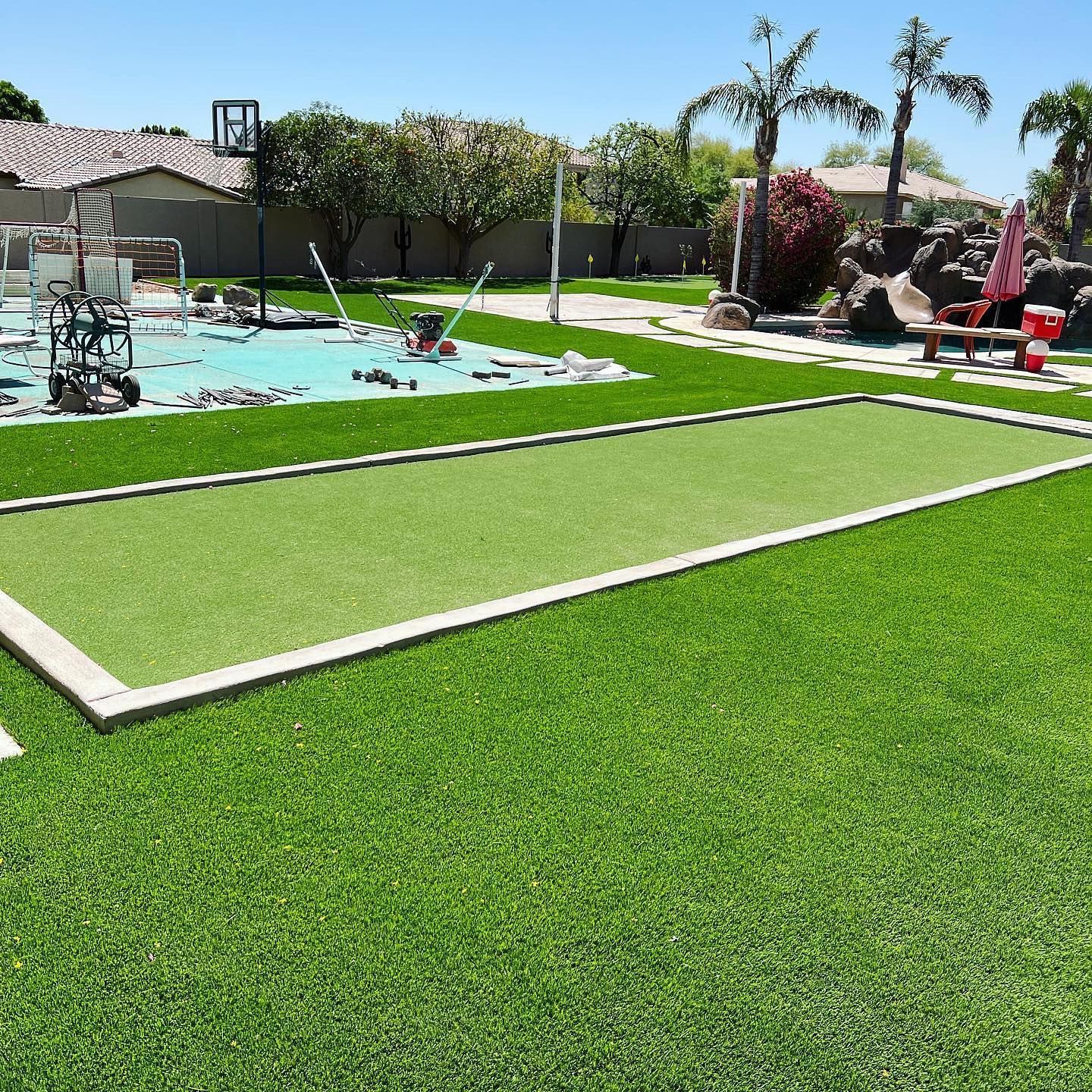 A lawn with a basketball hoop and a pool in the background.