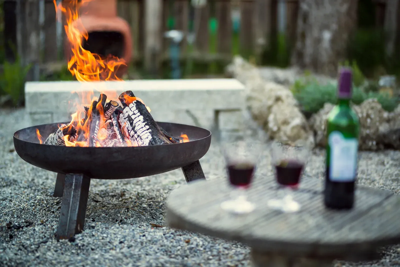 A fire pit with a bottle of wine and two glasses of wine on a table.