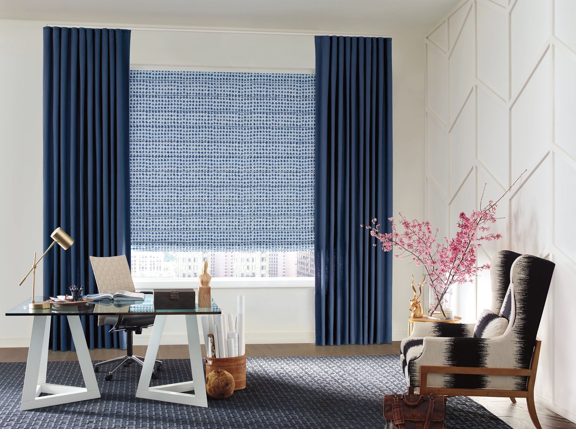 Office with blue curtains, patterned shades, desk with lamp, and patterned chair.