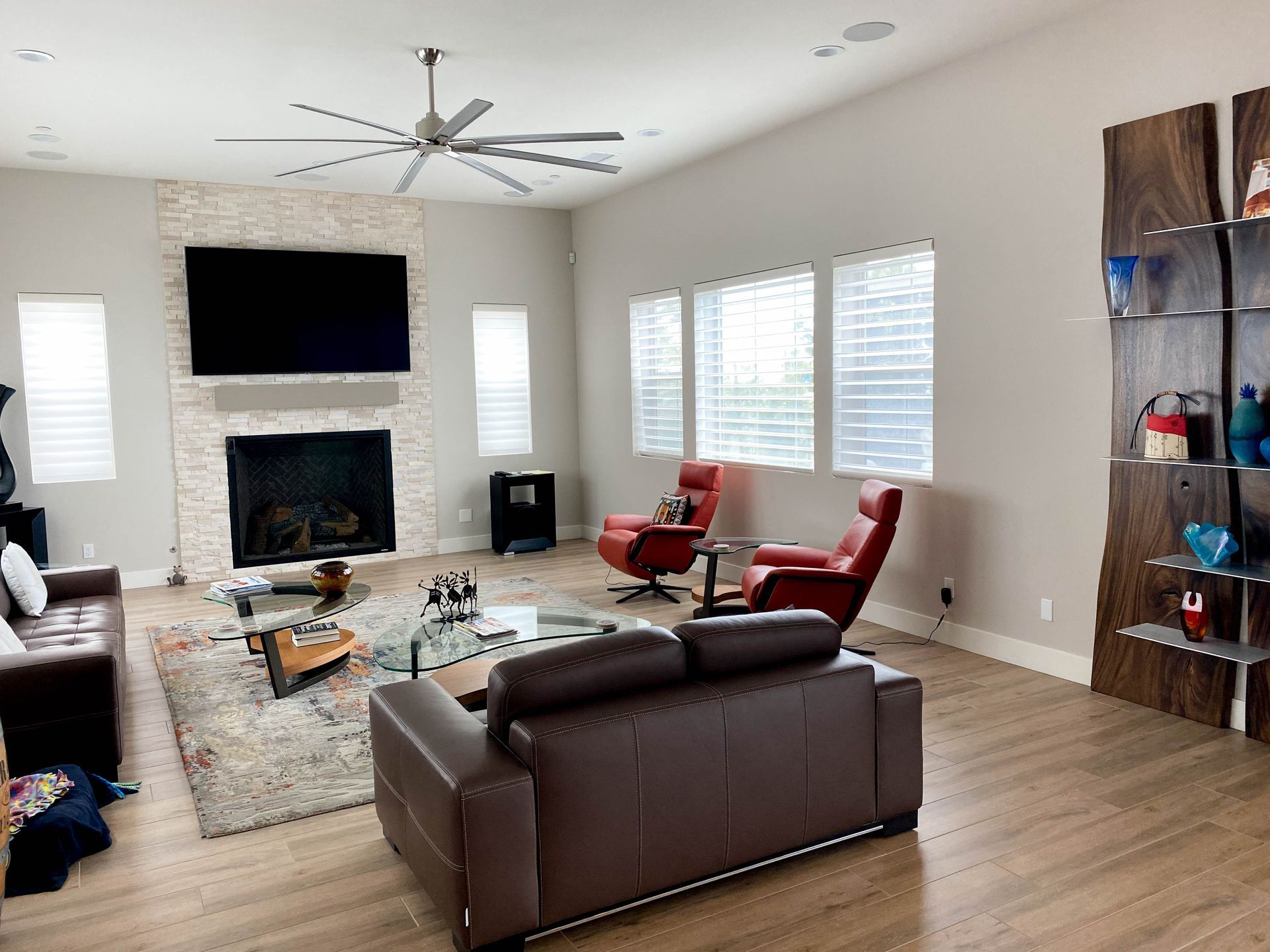 Living room with fireplace, TV, red chairs, brown leather sofas, and wooden shelving.