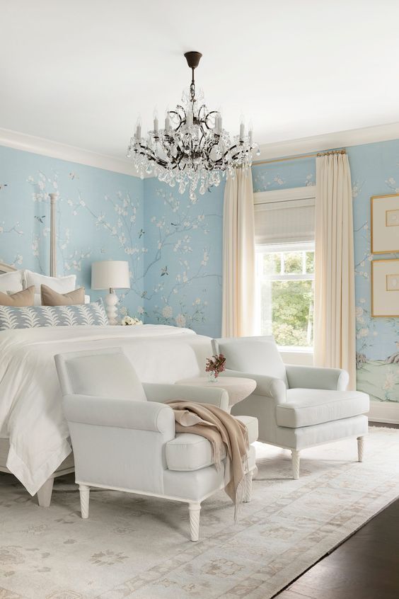 Elegant bedroom with blue floral wallpaper, white furniture, and a crystal chandelier.
