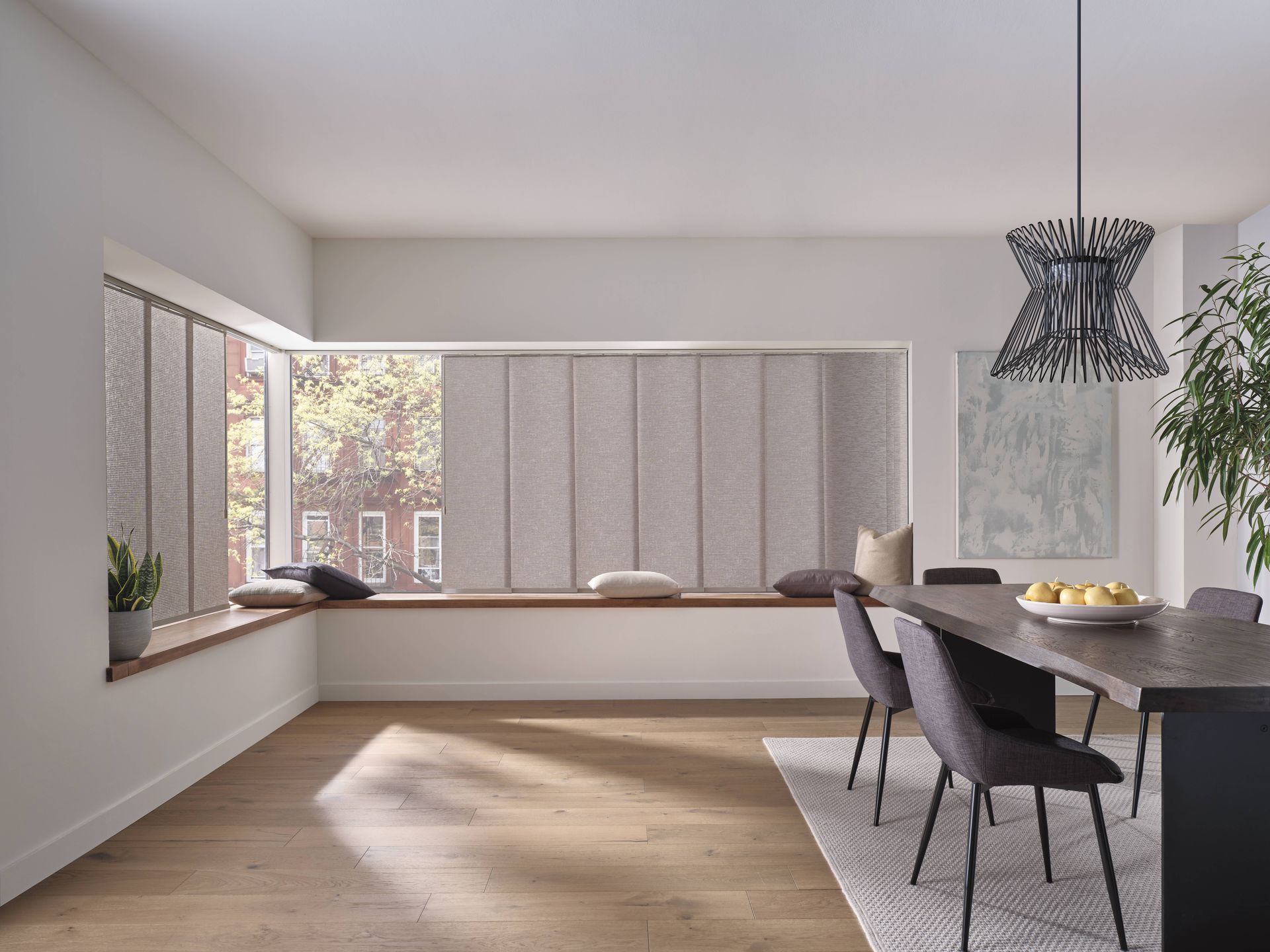 Dining room with window seat, vertical blinds, dark table, chairs, and modern light fixture.