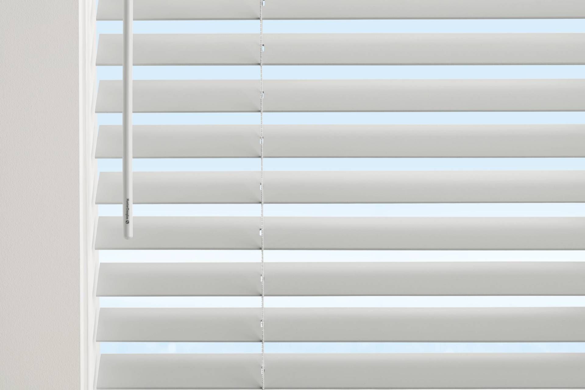 White venetian blinds partially covering a window, light shining through the slats.