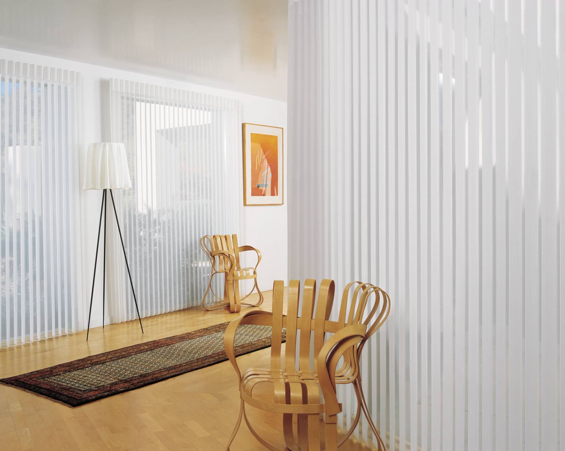 Bright room with white vertical blinds, chairs, a rug, and artwork. A floor lamp stands near the window.