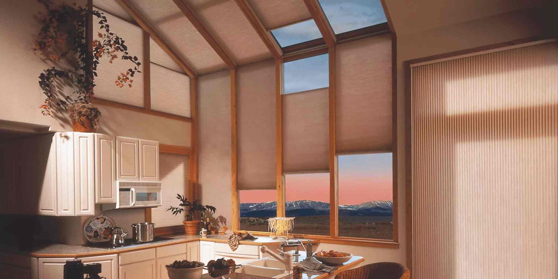 Kitchen with large windows, light-colored cabinets, and mountain view through the windows.