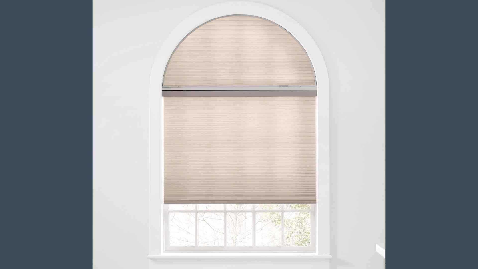 Arched window with beige cellular shades; white trim, set against a dark blue background.