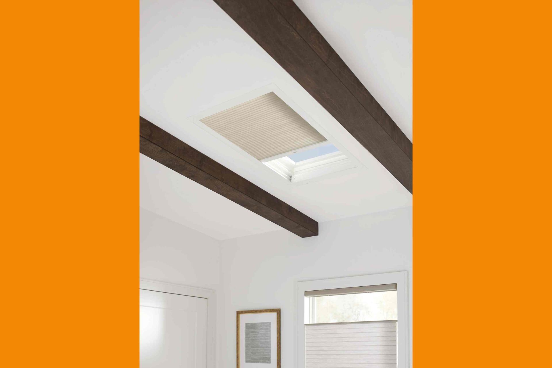 Skylight with beige honeycomb shade, framed by dark wood beams on a white ceiling.