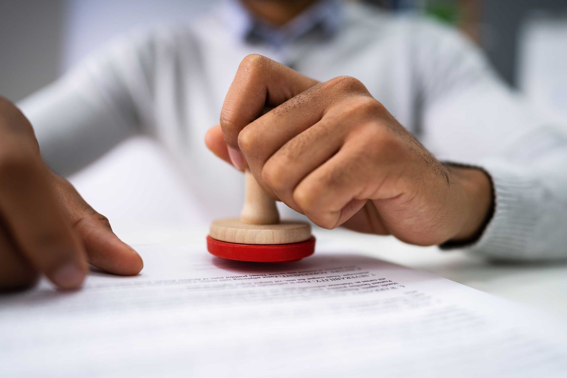 Person's hand stamping a red ink seal onto a white document.