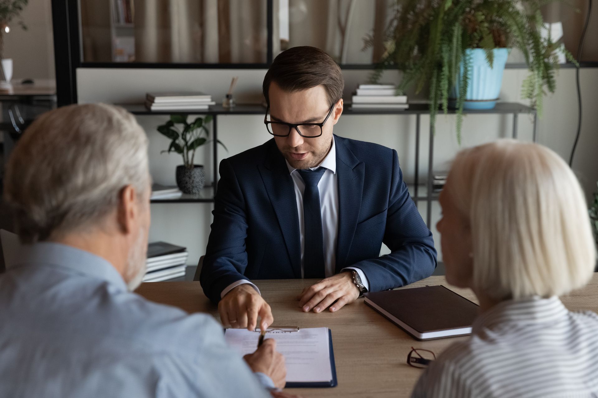 Man in suit pointing to document as older couple looks on.