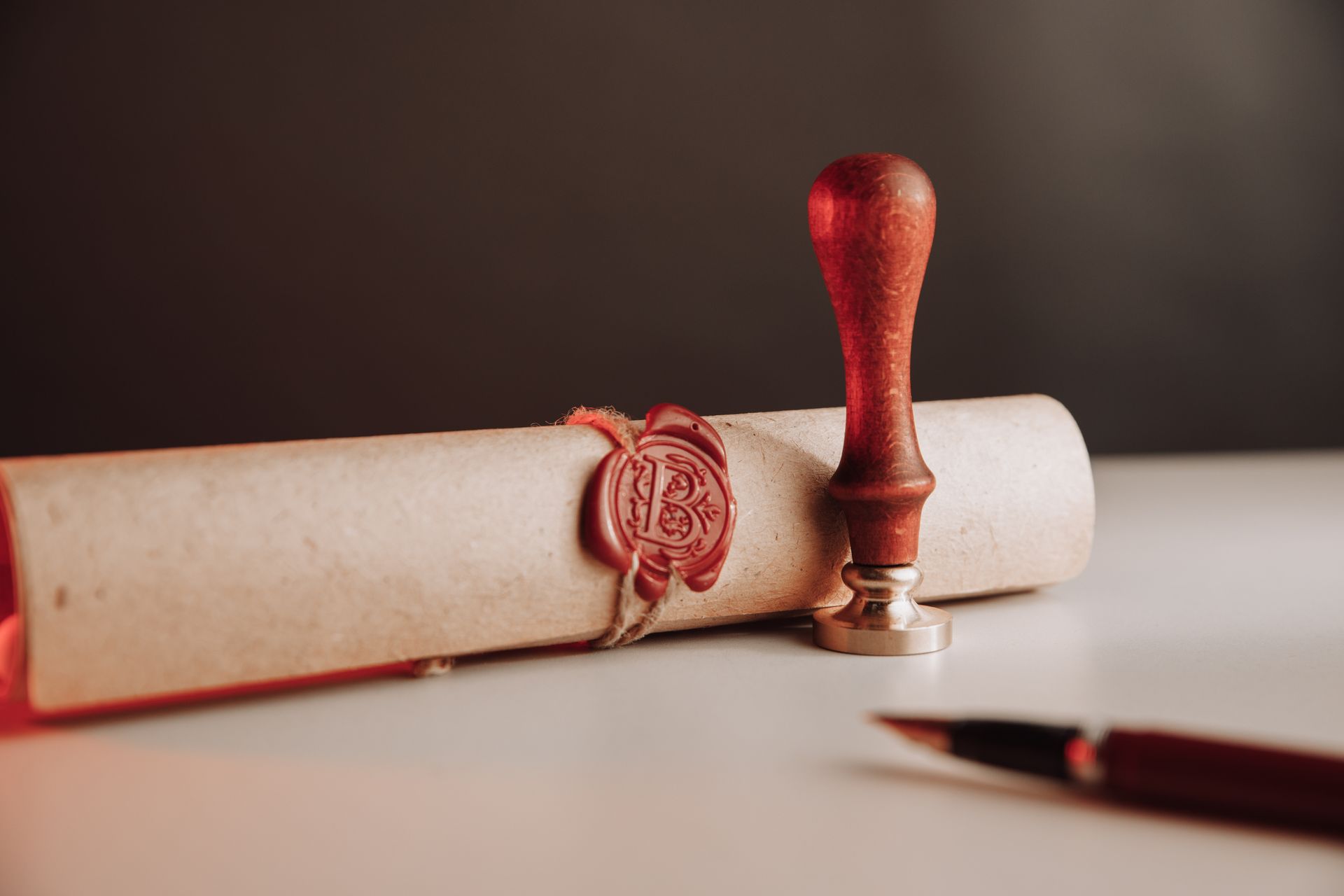 Parchment scroll sealed with wax, sealing stamp, and pen on a white surface with a dark background.