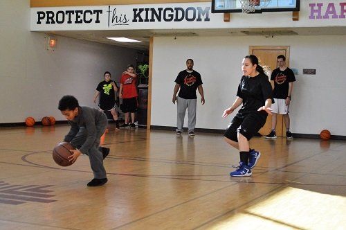 A group of people are playing basketball in front of a sign that says protect this kingdom