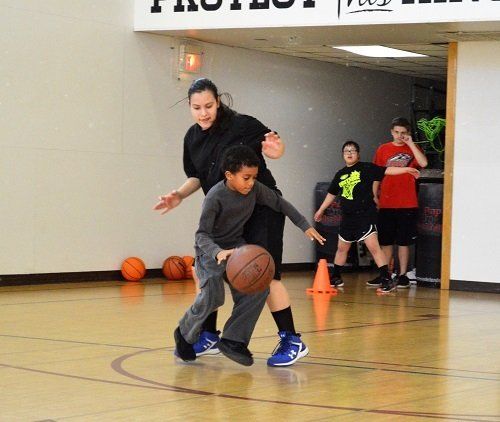 A boy dribbles a basketball while a woman watches