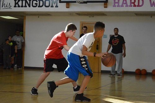 Two boys are playing basketball on a court with a sign that says this kingdom