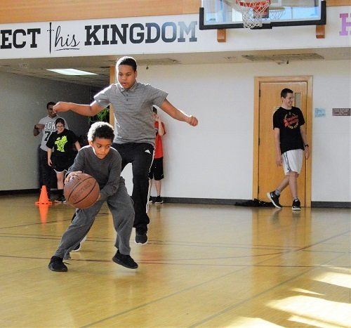A boy dribbles a basketball in front of a sign that says ect his kingdom
