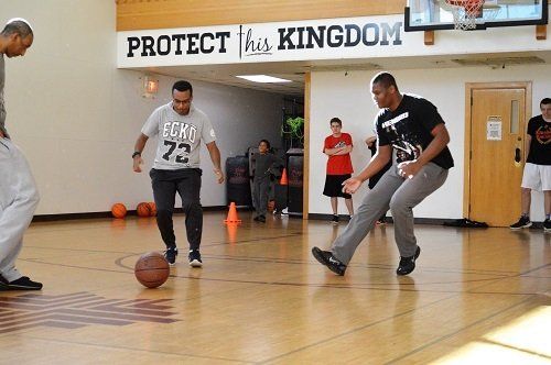 Men playing basketball in a gym with a sign that says protect his kingdom