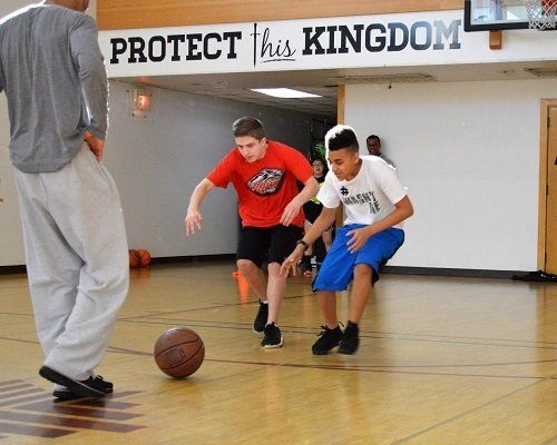 Three boys are playing basketball in front of a sign that says protect this kingdom